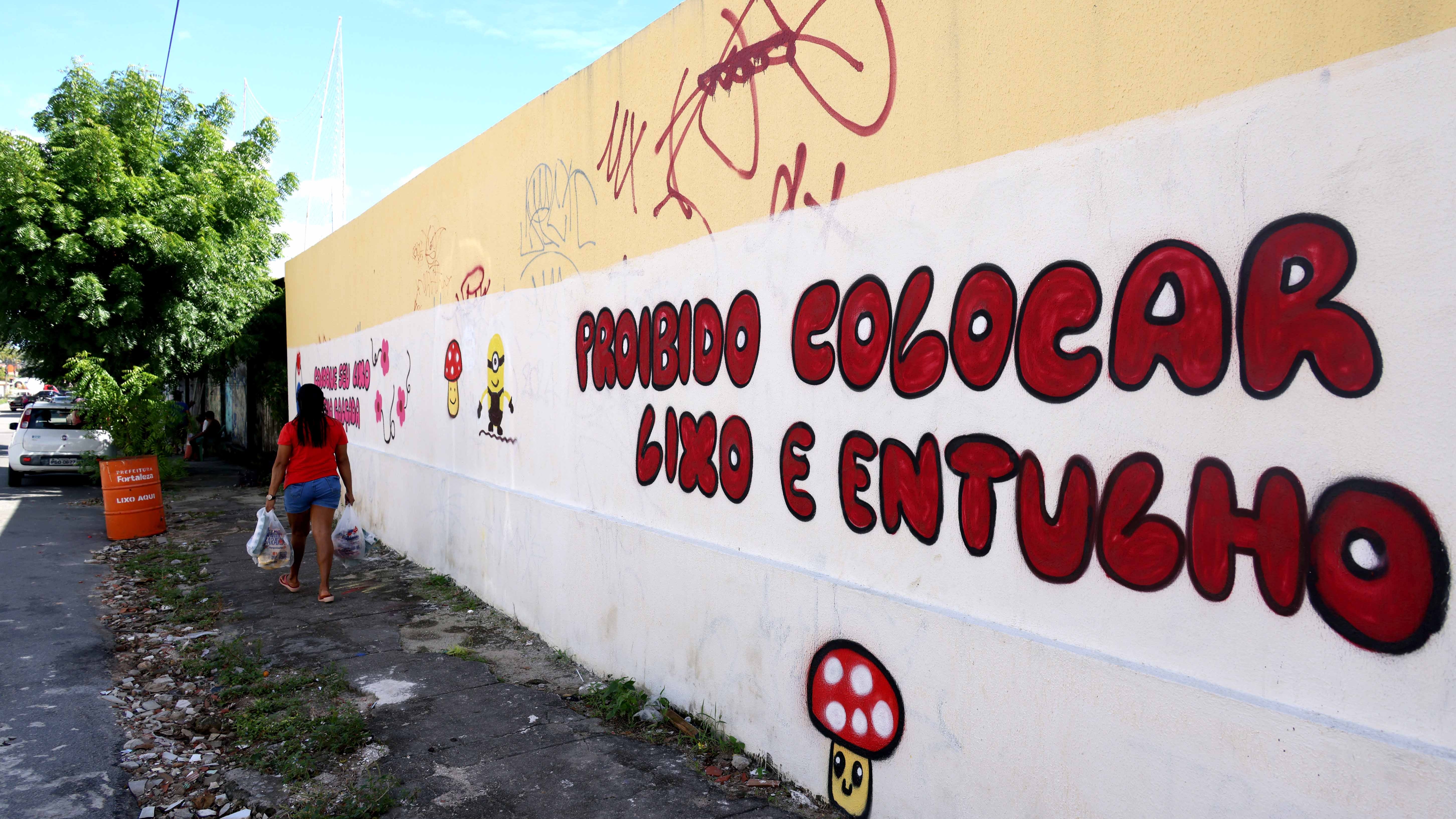 mulher caminha na calçada com sacos de lixo na mão em um local que foi limpo e requalificado